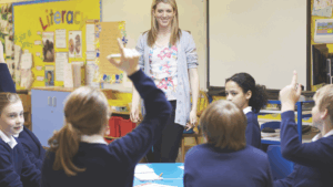 Smiling teacher looking across students with hands raised
