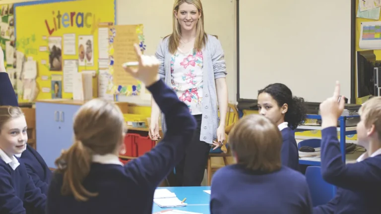 Smiling teacher looking across students with hands raised