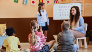 Teacher with students gathered around her, while one student stands at the front next to the board.