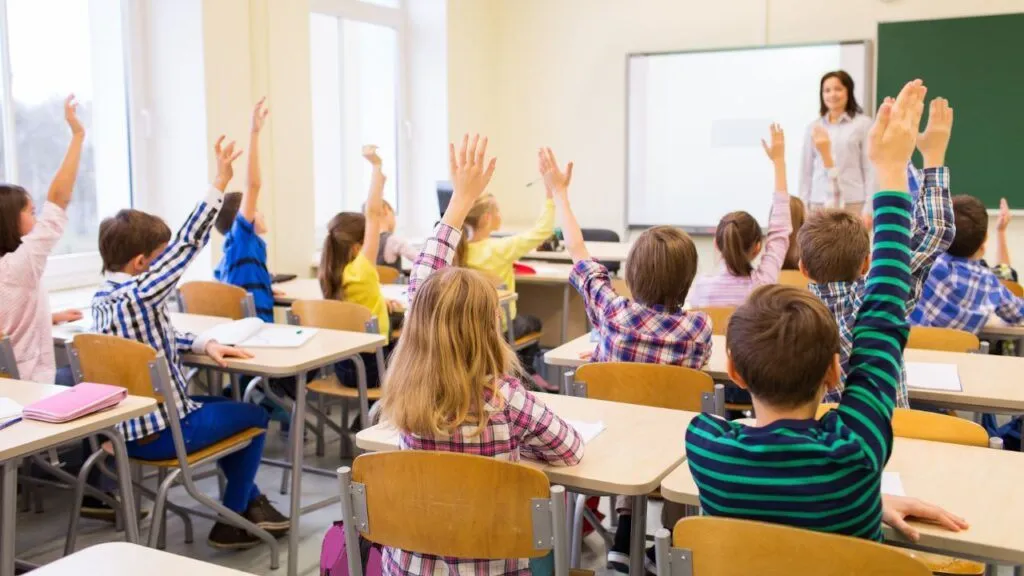 Classroom of students raising their hands to answer a question.