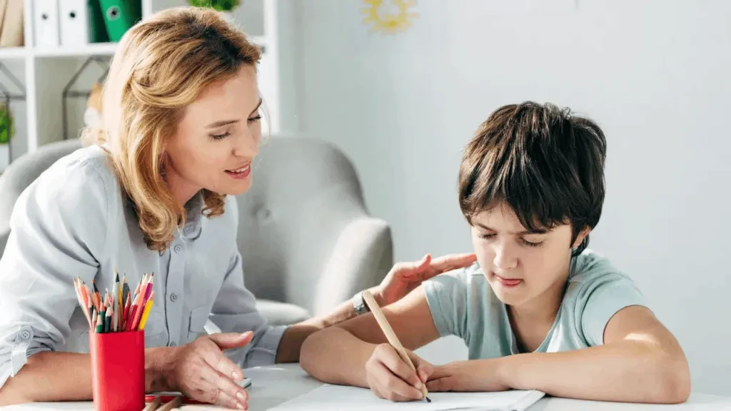 A teacher helping a student as he writes in his notebook.