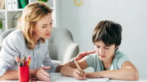 A teacher helping a student as he writes in his notebook.