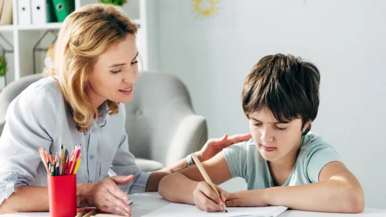 A teacher helping a student as he writes in his notebook.