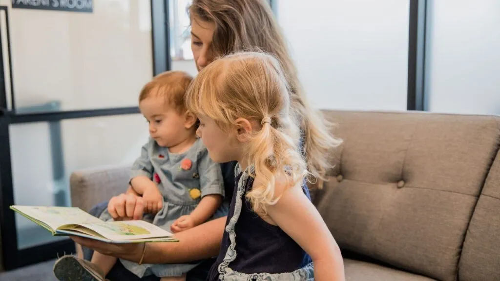 Mother sits with her two children while reading a book together