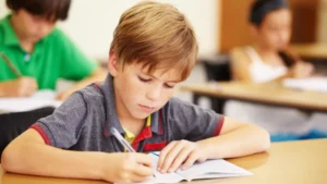 Young boy writes in a notebook at his desk